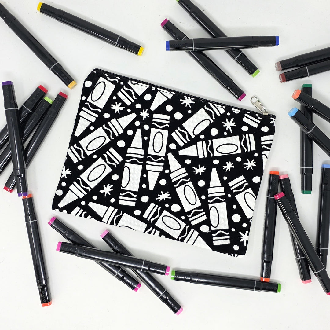 Photo of a black and white flat makeup bag with lots of colorful markers beside it indicating the customer gets to color it when they receive theirs. This is the same bag as the pencil case - Side A