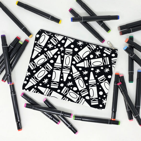 Photo of a black and white flat makeup bag with lots of colorful markers beside it indicating the customer gets to color it when they receive theirs. This is the same bag as the pencil case - Side A