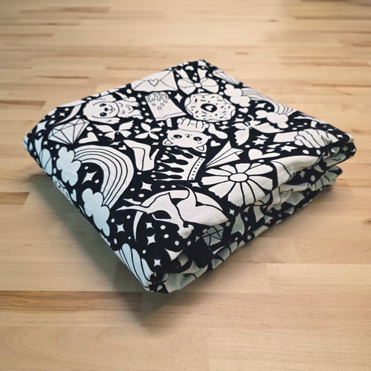 Uncolored version two doodle patterned blanket with donuts, cats, cupcakes patterned blanket folded on a table