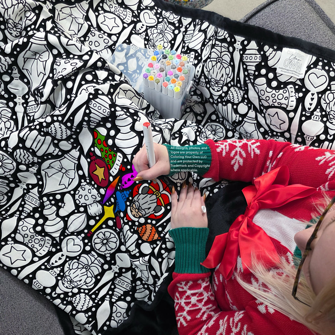 Person coloring a black and white patterned blanket with colorful markers
