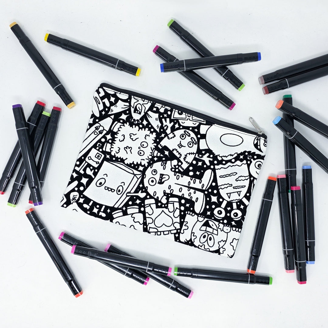 Photo of a black and white flat pencil pouch with lots of colorful markers beside it indicating the customer gets to color it when they receive theirs. This is the same bag as the pencil case and makeup bag - Side A - this bag has images of Coquette-inspired illustrations including a swan, a paw print, bows, a moon, stars, a bunny on it cherries and more