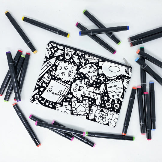 Photo of a black and white flat pencil pouch with lots of colorful markers beside it indicating the customer gets to color it when they receive theirs. This is the same bag as the pencil case and makeup bag - Side A - this bag has images of Coquette-inspired illustrations including a swan, a paw print, bows, a moon, stars, a bunny on it cherries and more