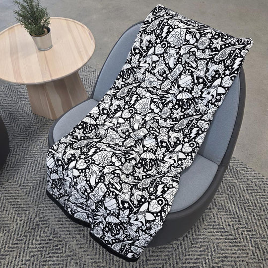 Black and white uncolored classic tattoo styles and patterns blanket with a black fleece lined underside draped over a gray chair.