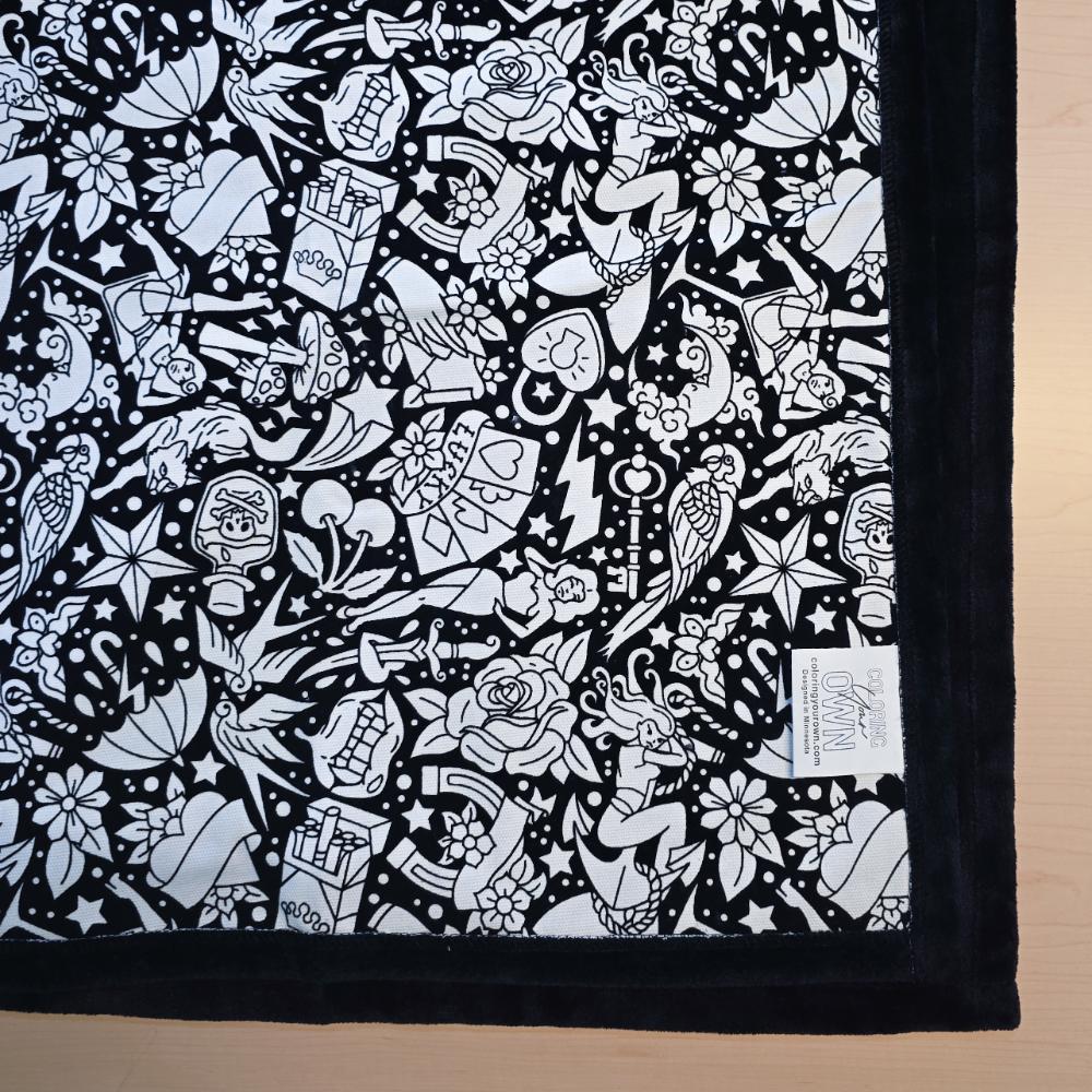 Black and white uncolored classic tattoo styles and patterns blanket with black fleece lined underside close up view