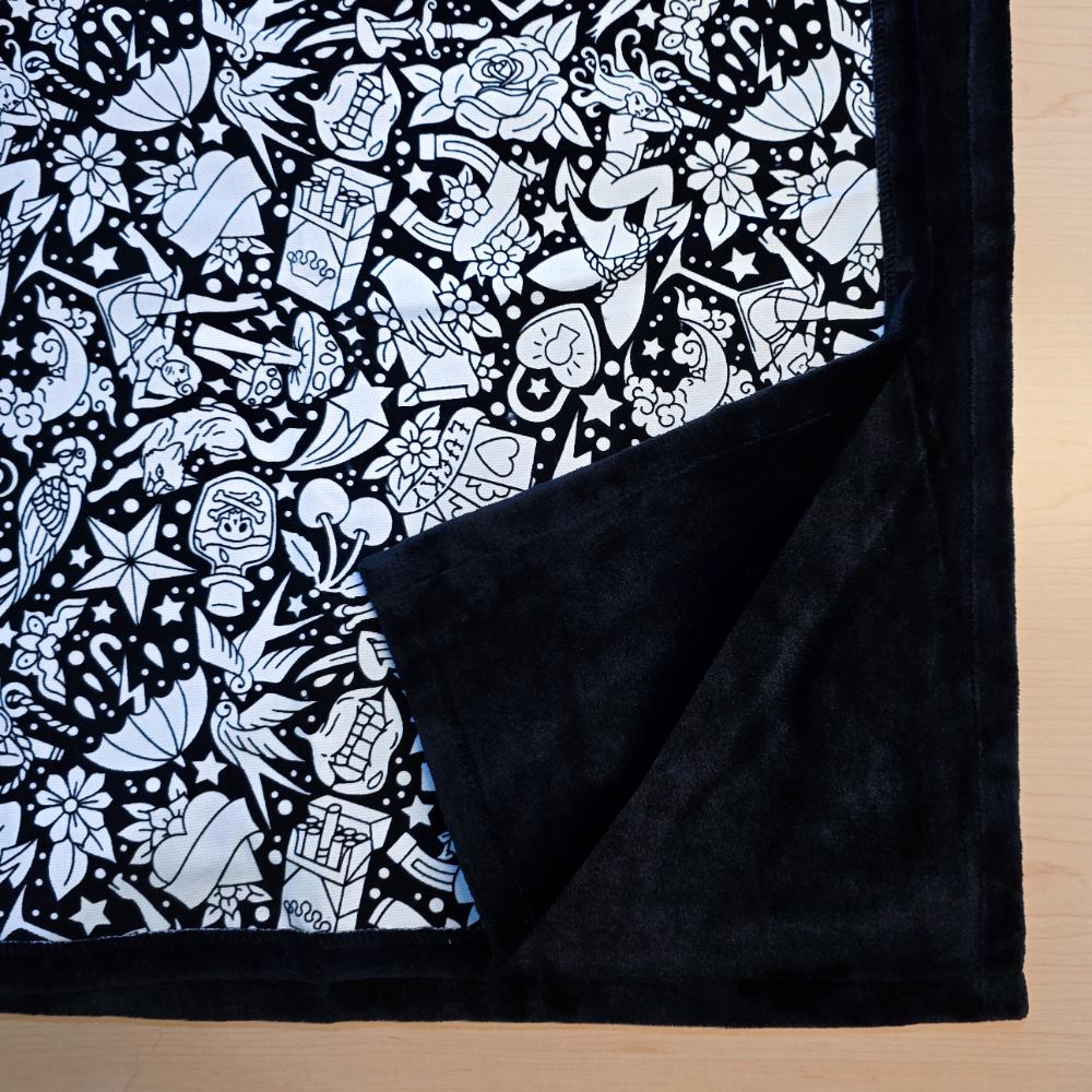 Black and white uncolored classic tattoo styles and patterns blanket with close up view showing black fleece lined underside