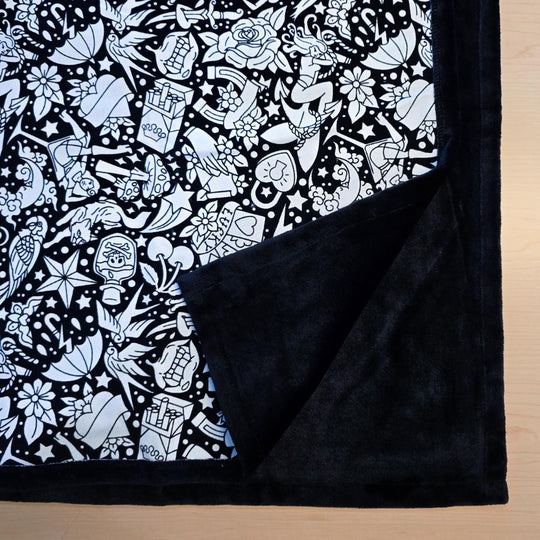 Black and white uncolored classic tattoo styles and patterns blanket with close up view showing black fleece lined underside