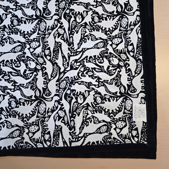 Black and white uncolored dinosaurs with dinosaur eggs patterned blanket with black fleece lined underside close up view