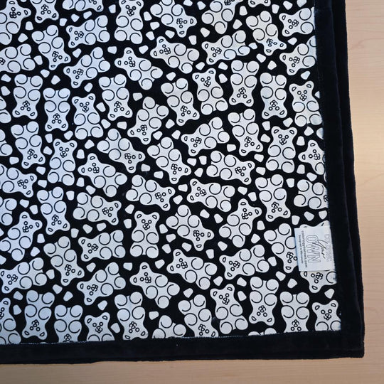 Black and white uncolored gummy bears and gumdrops patterned blanket with black fleece lined underside close up view