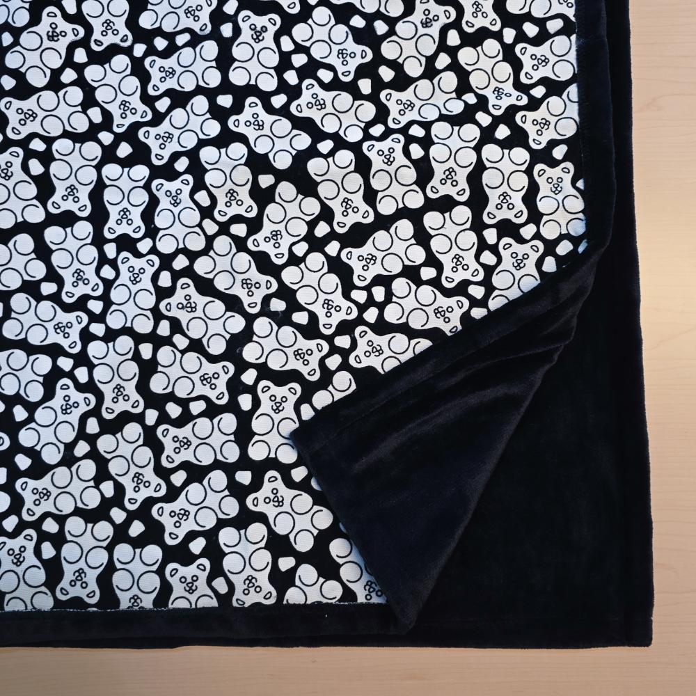 Black and white uncolored gummy bears and gumdrops patterned blanket with close up view showing black fleece lined underside