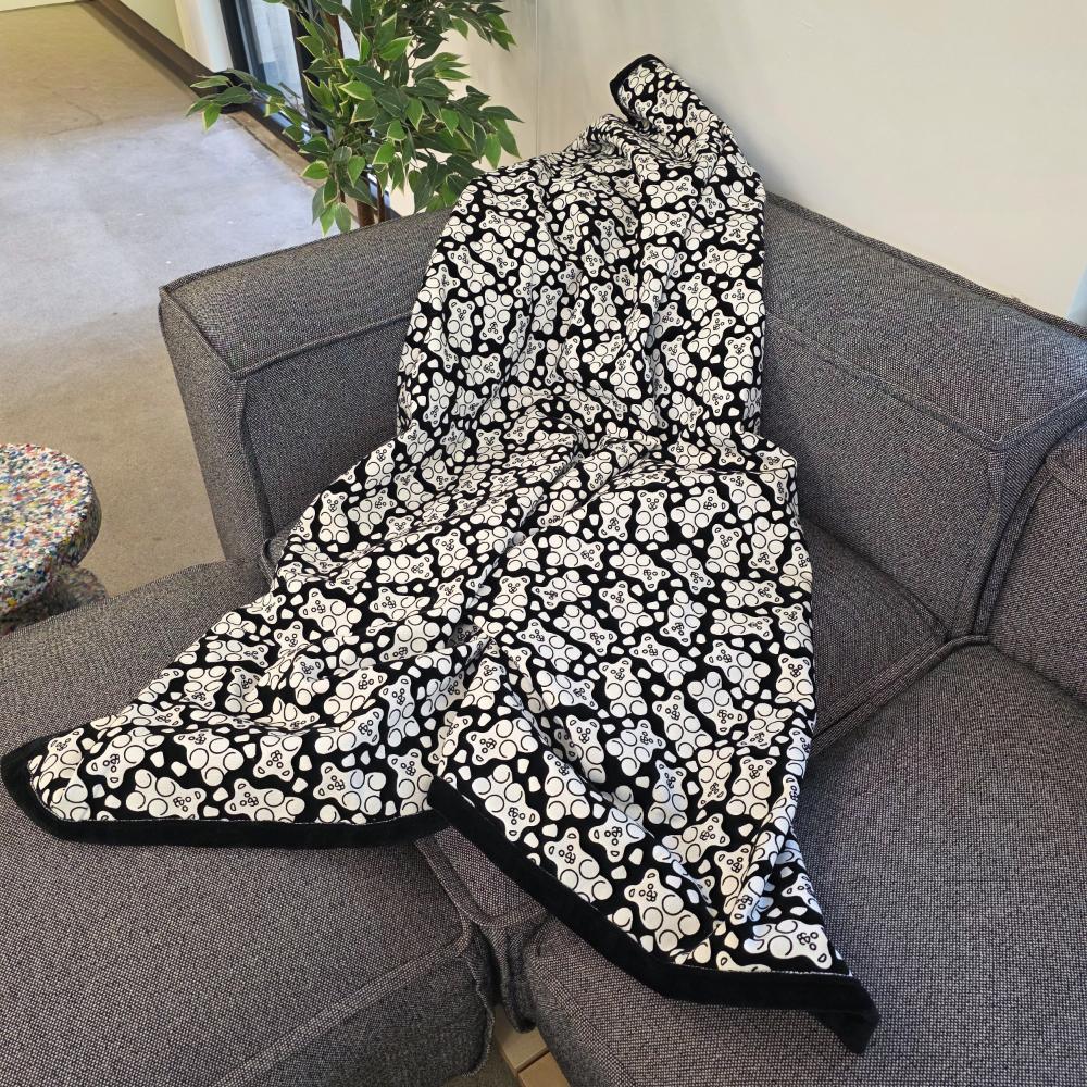 Black and white uncolored gummy bears and gumdrops patterned blanket with a black fleece lined underside draped over a gray couch.