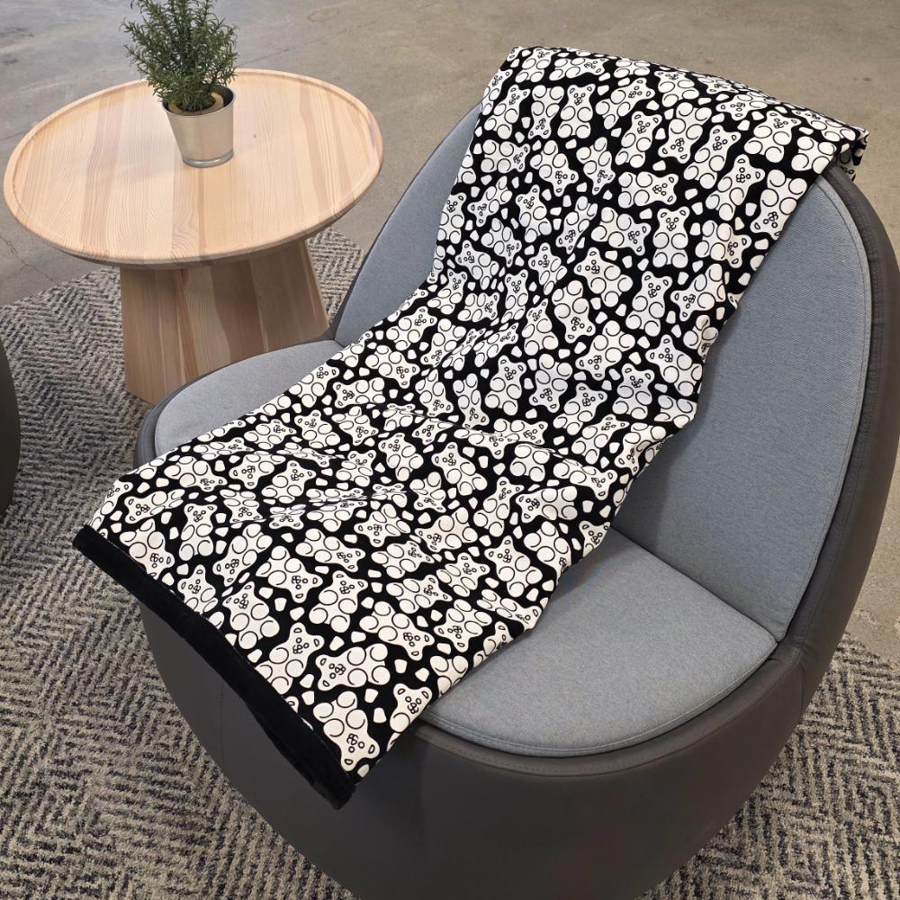 Black and white uncolored gummy bears and gumdrops patterned blanket with a black fleece lined underside draped over a gray chair.