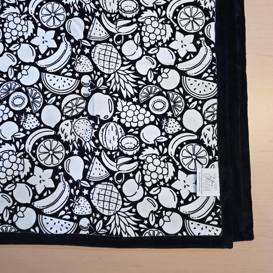 Black and white uncolored fruit variety with pineapples, bananas, watermelons and more patterned blanket with black fleece lined underside close up view