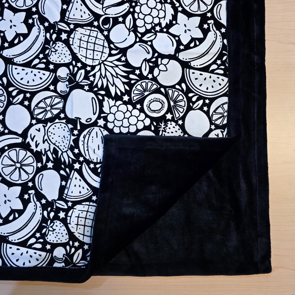 Black and white uncolored fruit variety with pineapples, bananas, watermelons and more patterned blanket with close up view showing black fleece lined underside