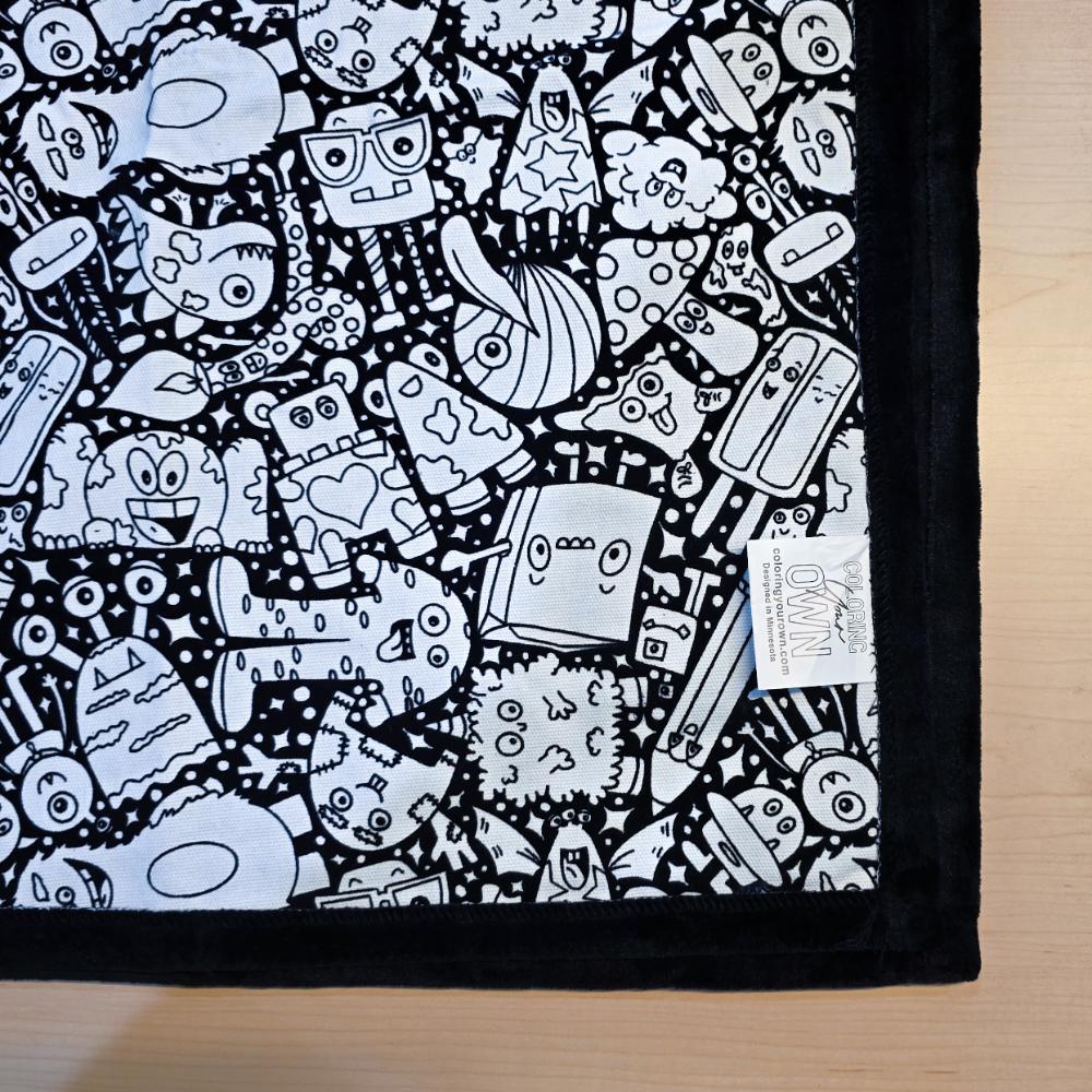 Black and white uncolored  silly monster party patterned blanket with black fleece lined underside close up view