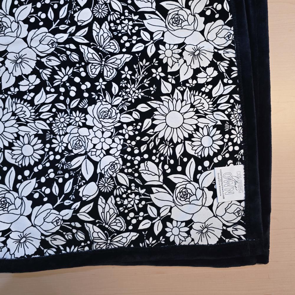 Black and white uncolored vintage floral and butterfly patterned blanket with black fleece lined underside close up view