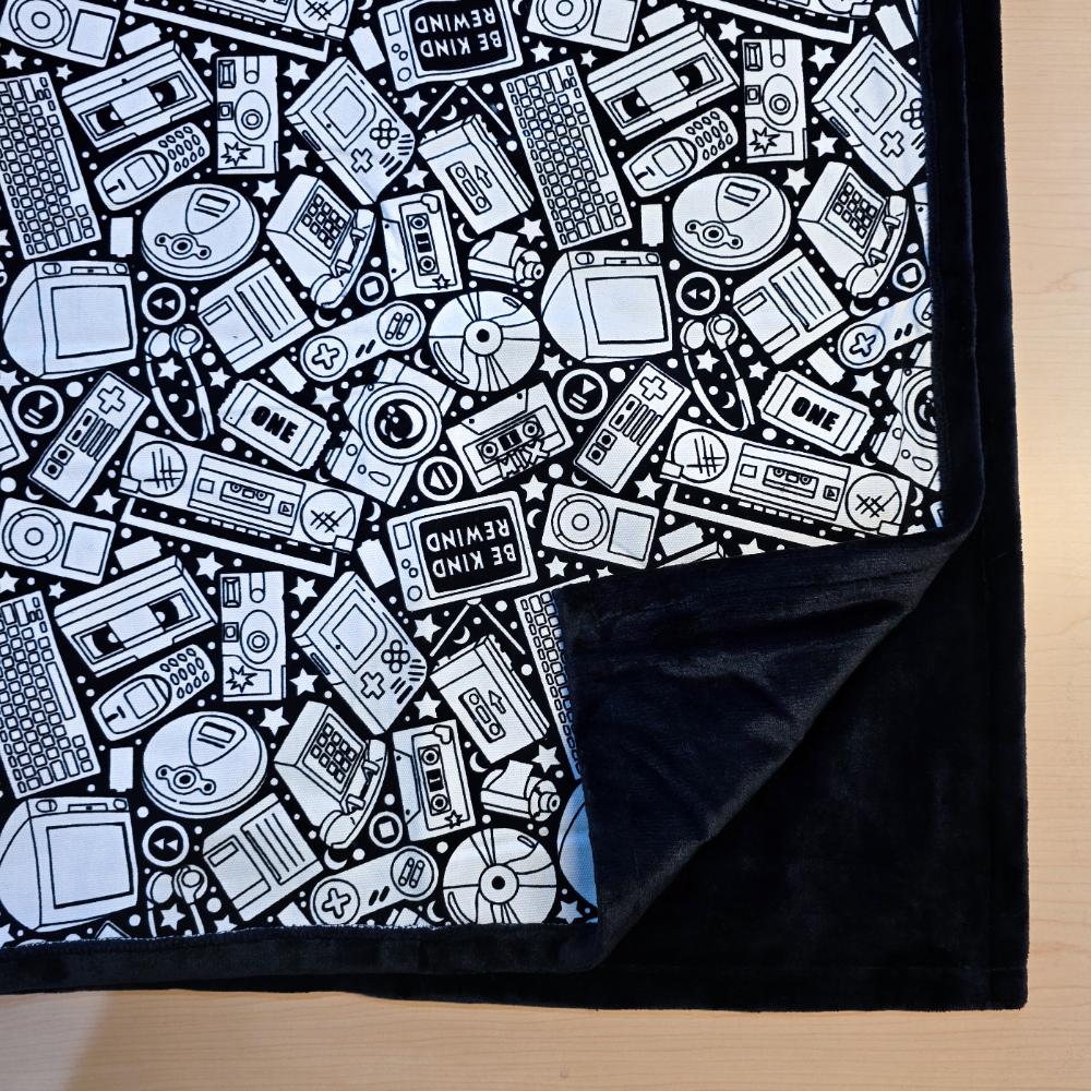 Black and white uncolored retro technology, keyboard ,camera and stereo patterned blanket with close up view showing black fleece lined underside