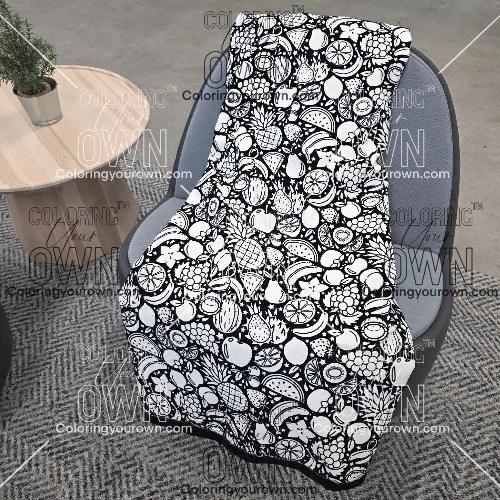 Black and white uncolored fruit variety with pineapples, bananas, watermelons and more patterned blanket with a black fleece lined underside draped over a gray chair.