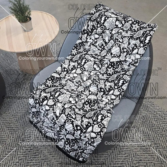 Black and white uncolored classic tattoo styles and patterns blanket with a black fleece lined underside draped over a gray chair.
