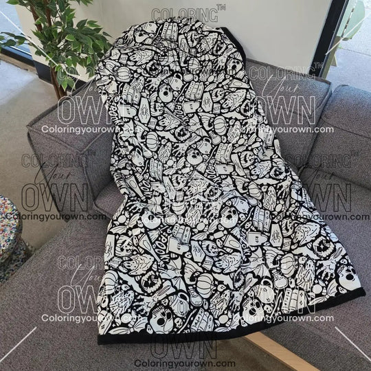 Black and white uncolored spooky halloween patterned blanket with skulls and bats and a black fleece lined underside draped over a gray couch.