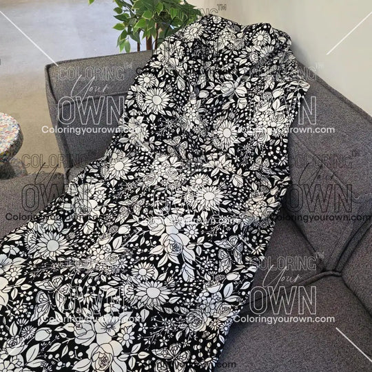 Black and white uncolored vintage floral and butterfly patterned blanket with a black fleece lined underside draped over a gray couch.