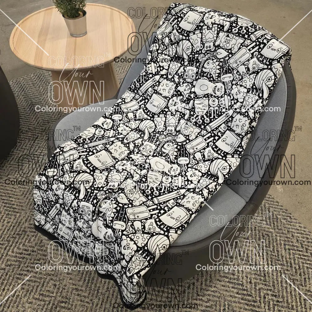 Black and white uncolored silly monster party patterned blanket with black fleece lined underside draped over a gray chair.
