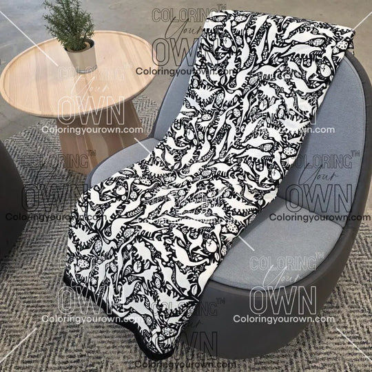 Black and white uncolored dinosaurs with dinosaur eggs patterned blanket with a black fleece lined underside draped over a gray chair.