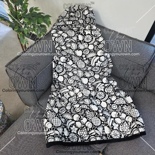 Black and white uncolored fruit variety with pineapples, bananas, watermelons and more patterned blanket with a black fleece lined underside draped over a gray couch.