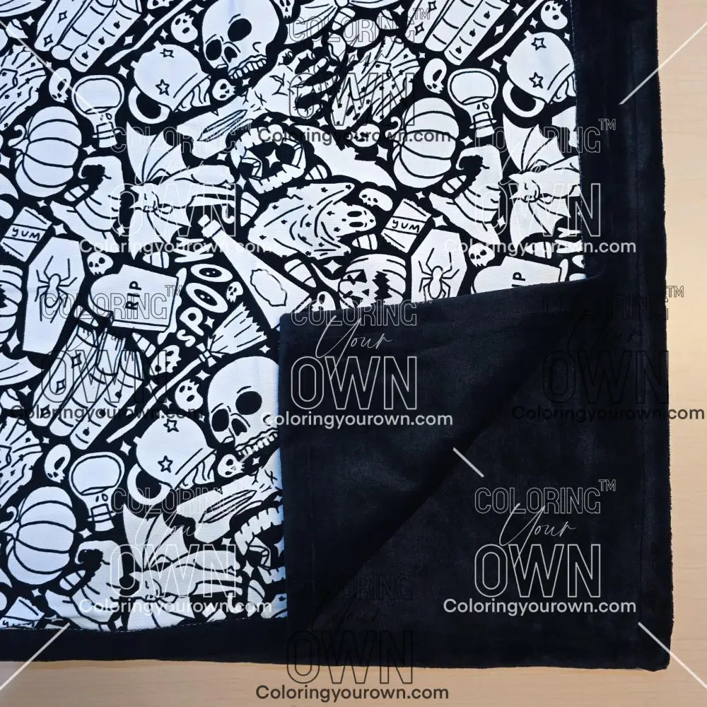 Black and white uncolored spooky Halloween patterned blanket with skulls, ghosts and pumpkins with close up view showing black fleece lined underside