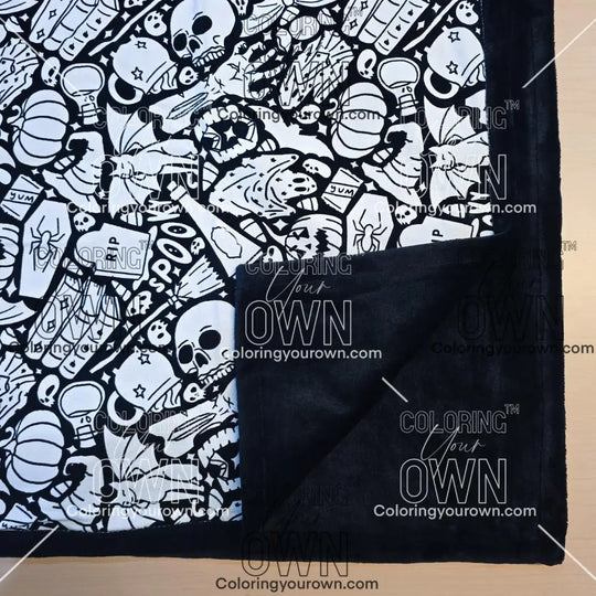 Black and white uncolored spooky Halloween patterned blanket with skulls, ghosts and pumpkins with close up view showing black fleece lined underside