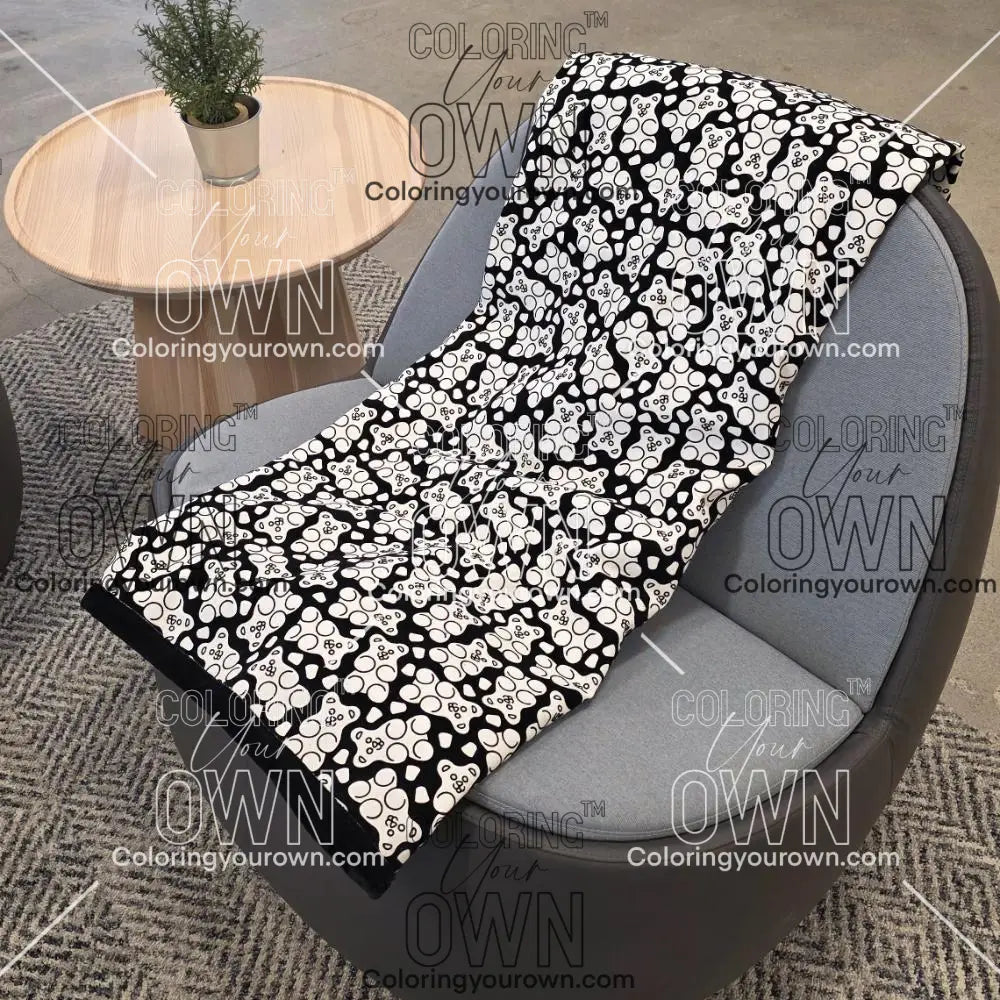 Black and white uncolored gummy bears and gumdrops patterned blanket with a black fleece lined underside draped over a gray chair.