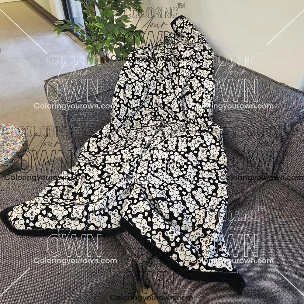 Black and white uncolored gummy bears and gumdrops patterned blanket with a black fleece lined underside draped over a gray couch.