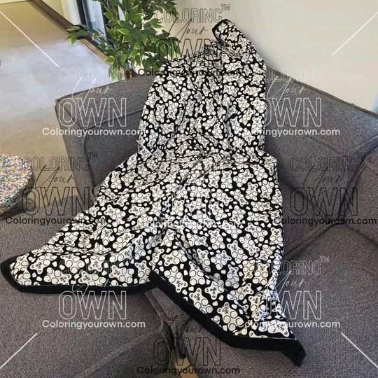 Black and white uncolored gummy bears and gumdrops patterned blanket with a black fleece lined underside draped over a gray couch.