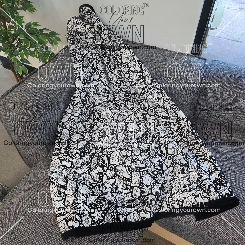 Black and white uncolored classic tattoo styles and patterns blanket with a black fleece lined underside draped over a gray couch.