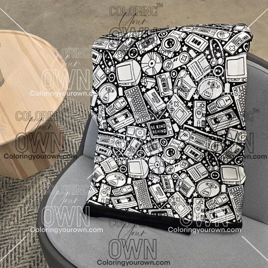 Black and white uncolored retro technology, keyboard ,camera and stereo patterned blanket with a black fleece lined underside draped over a gray chair.