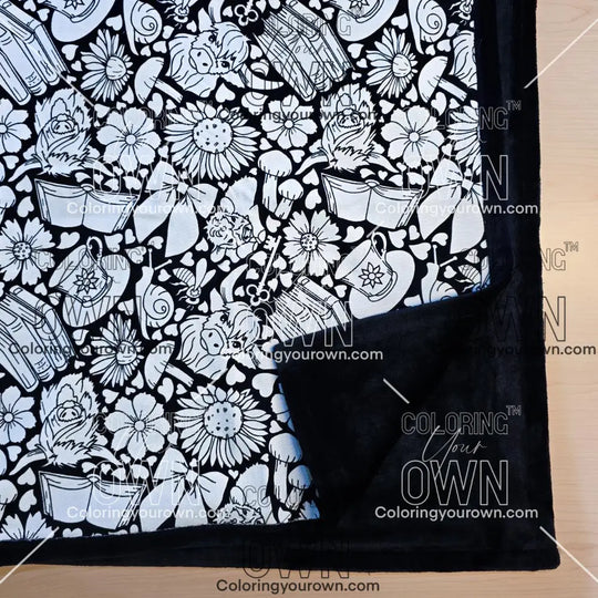 Black and white uncolored highland cow with books and tea patterned blanket with close up view showing black fleece lined underside