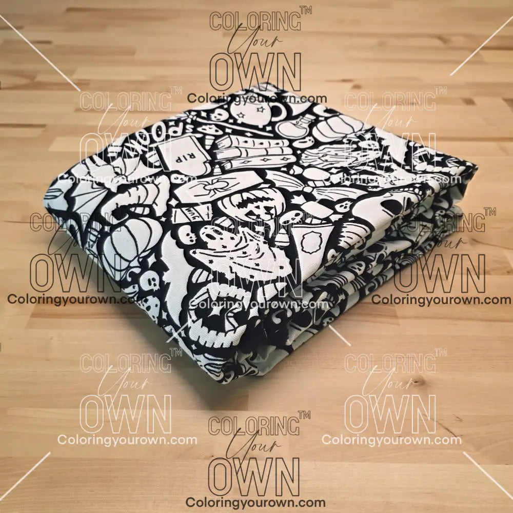 Uncolored Spooky Halloween blanket with ghosts, skulls, pumpkins, and other themed images folded on a table