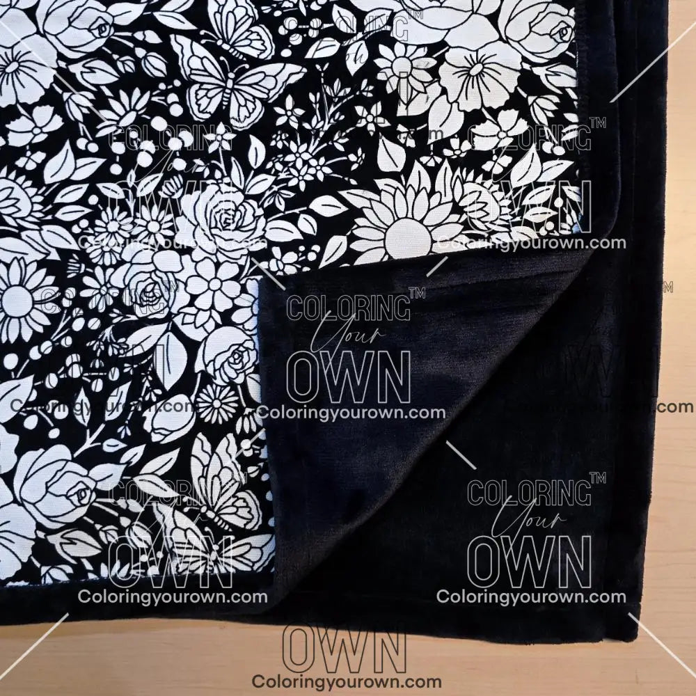 Black and white uncolored vintage floral and butterfly patterned blanket with close up view showing black fleece lined underside