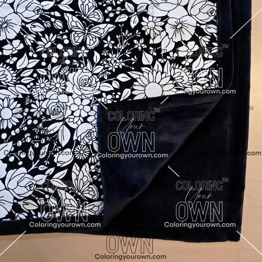 Black and white uncolored vintage floral and butterfly patterned blanket with close up view showing black fleece lined underside
