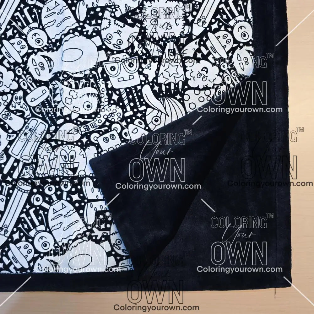 Black and white uncolored silly monster party patterned blanket with close up view showing black fleece lined underside