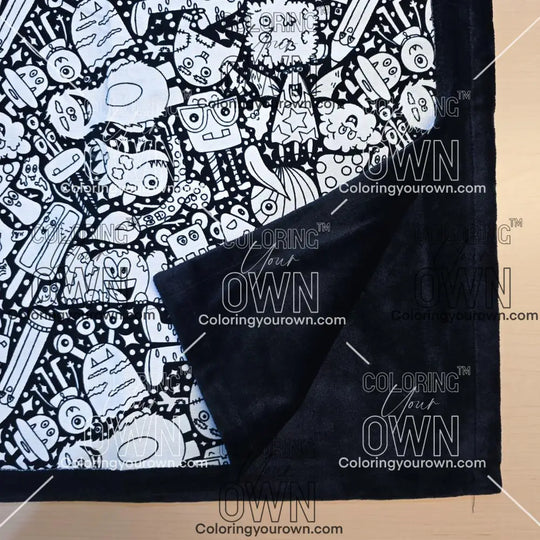 Black and white uncolored silly monster party patterned blanket with close up view showing black fleece lined underside