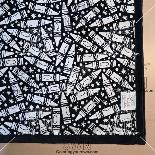 Black and white uncolored many crayon patterned blanket with black fleece lined underside close up view