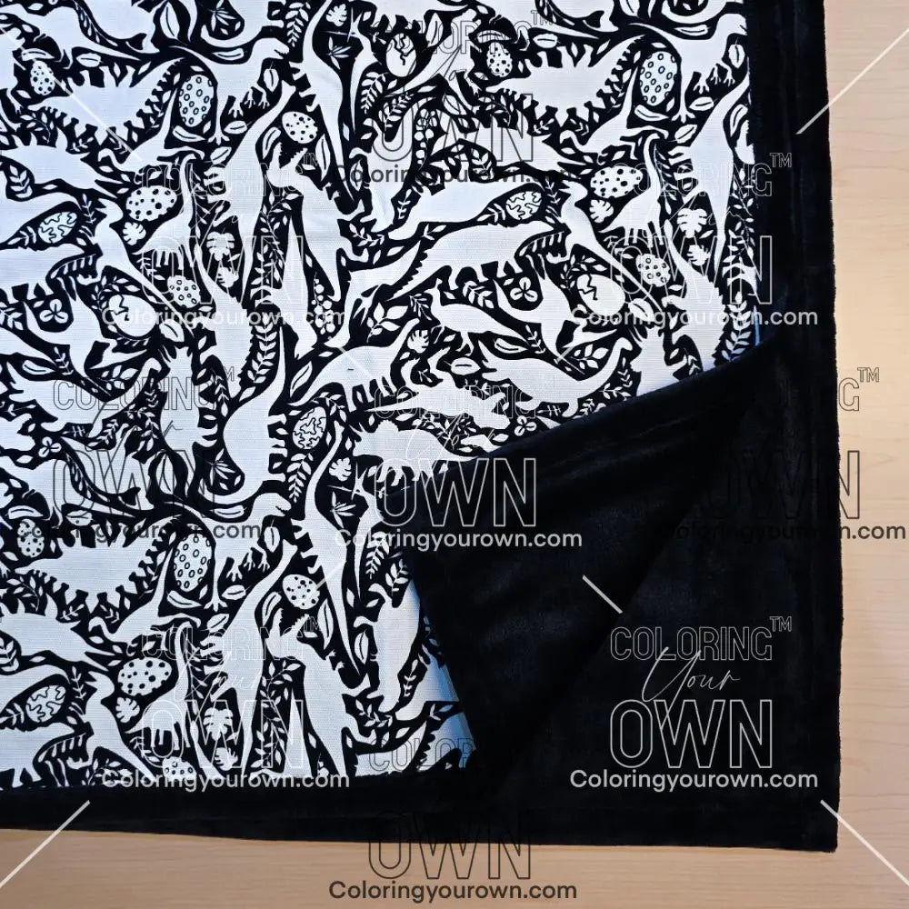 Black and white uncolored dinosaurs with dinosaur eggs patterned blanket with close up view showing black fleece lined underside