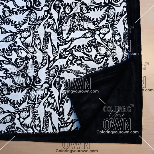 Black and white uncolored dinosaurs with dinosaur eggs patterned blanket with close up view showing black fleece lined underside
