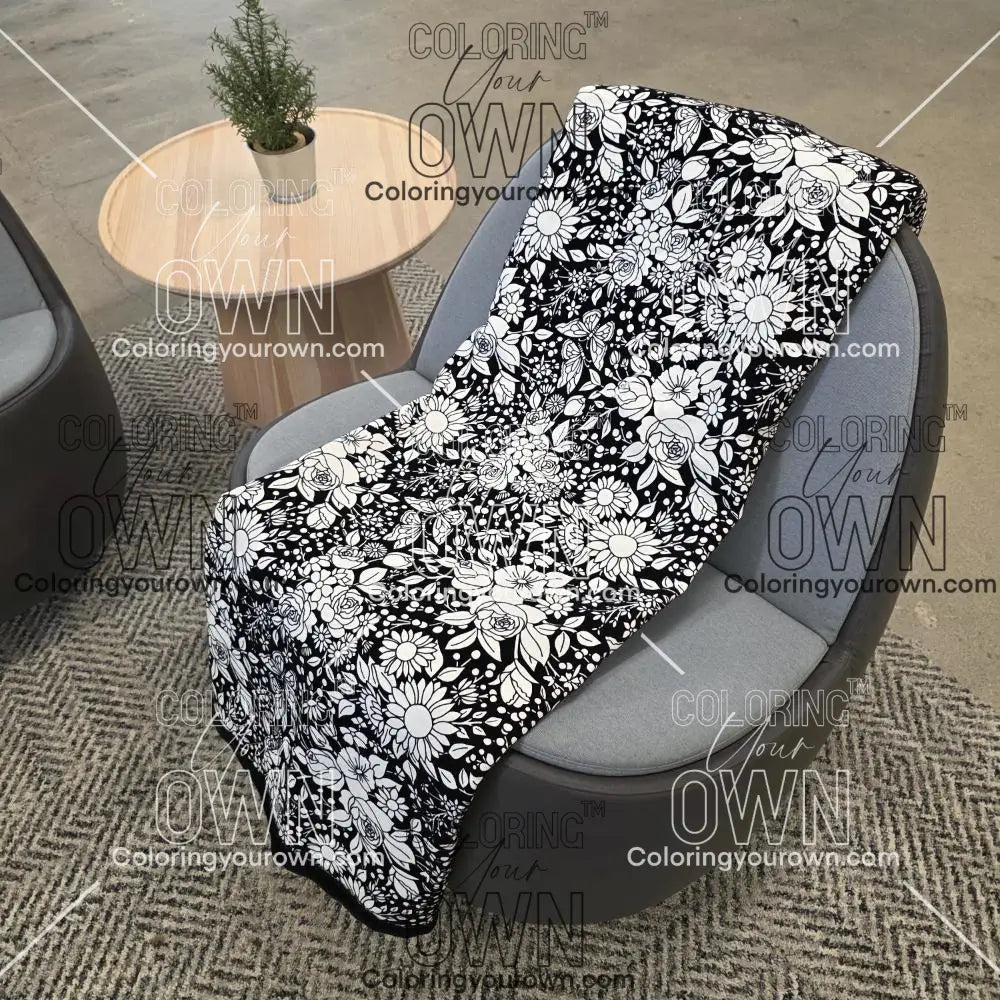 Black and white uncolored vintage floral and butterfly patterned blanket with a black fleece lined underside draped over a gray chair.
