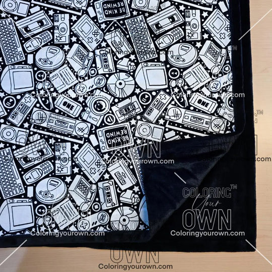 Black and white uncolored retro technology, keyboard ,camera and stereo patterned blanket with close up view showing black fleece lined underside