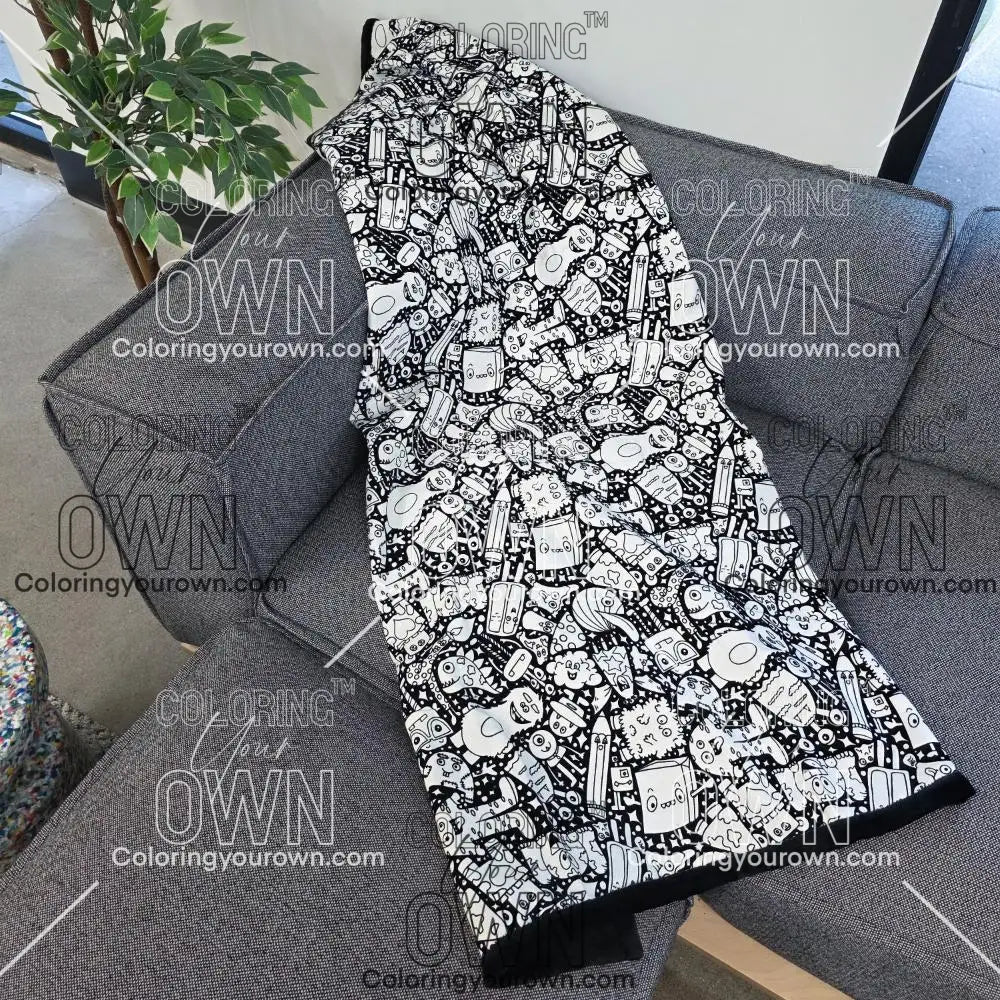 Black and white uncolored silly monster party patterned blanket with black fleece lined underside draped over a gray couch.