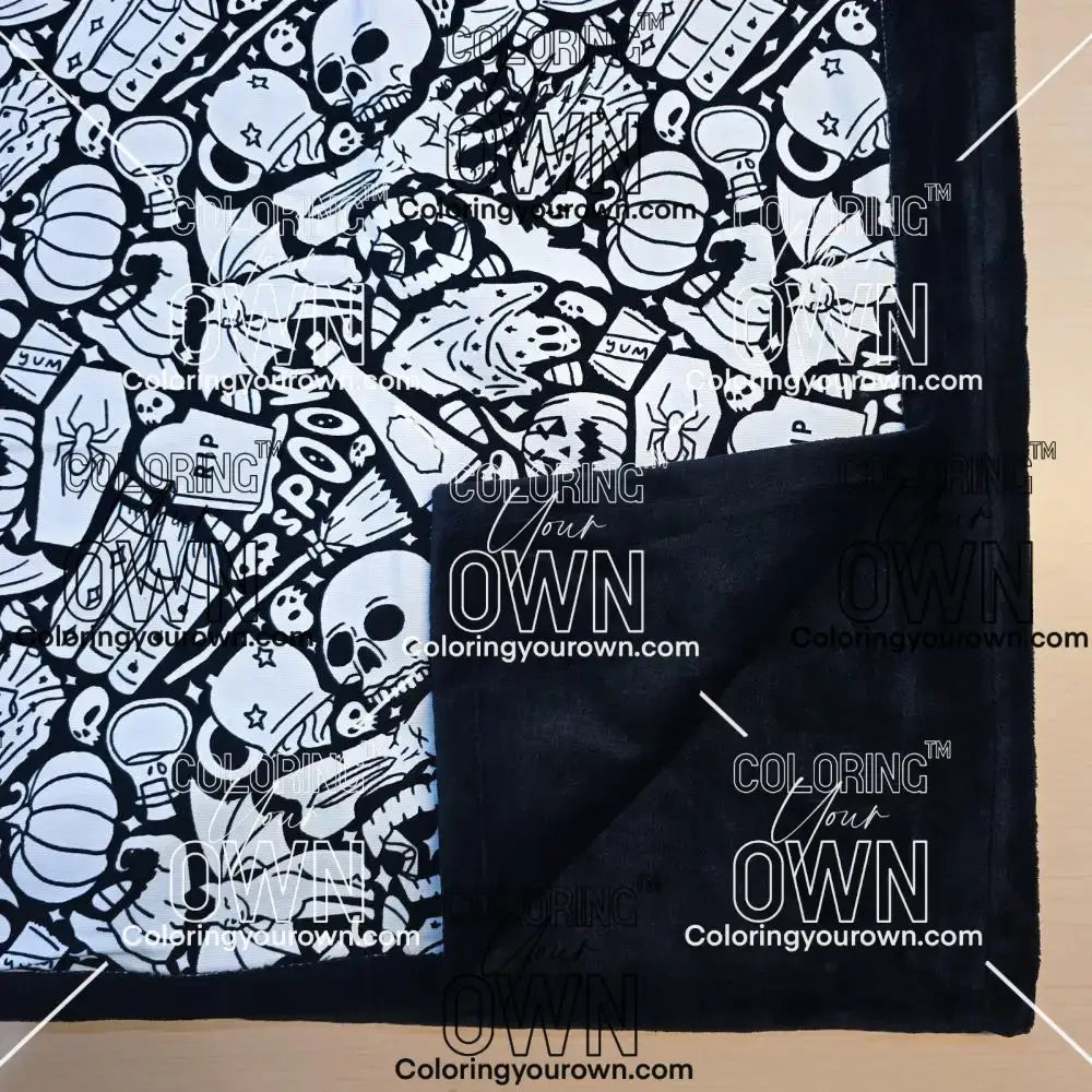 Black and white uncolored spooky Halloween patterned blanket with skulls, ghosts and pumpkins with close up view showing black fleece lined underside