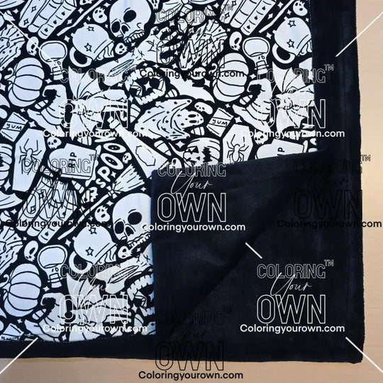 Black and white uncolored spooky Halloween patterned blanket with skulls, ghosts and pumpkins with close up view showing black fleece lined underside