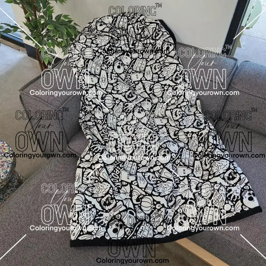 Black and white uncolored spooky halloween patterned blanket with skulls and bats and a black fleece lined underside draped over a gray couch.