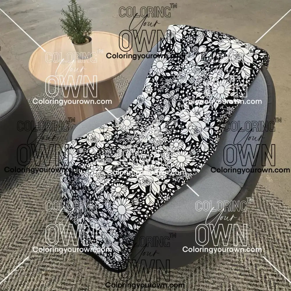 Black and white uncolored vintage floral and butterfly patterned blanket with a black fleece lined underside draped over a gray chair.